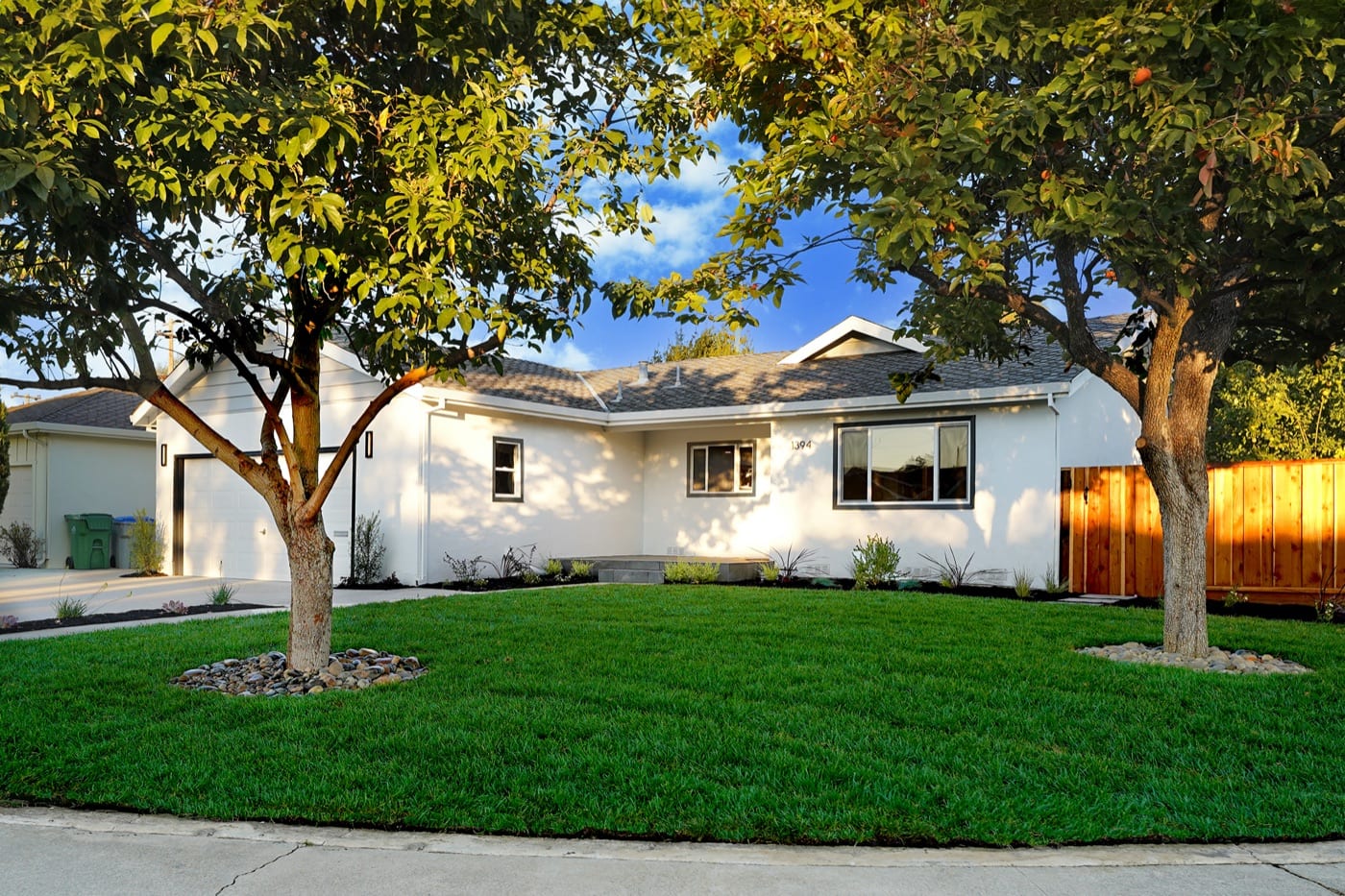 After: freshly painted white ranch home with new lawn, fence and landscaping