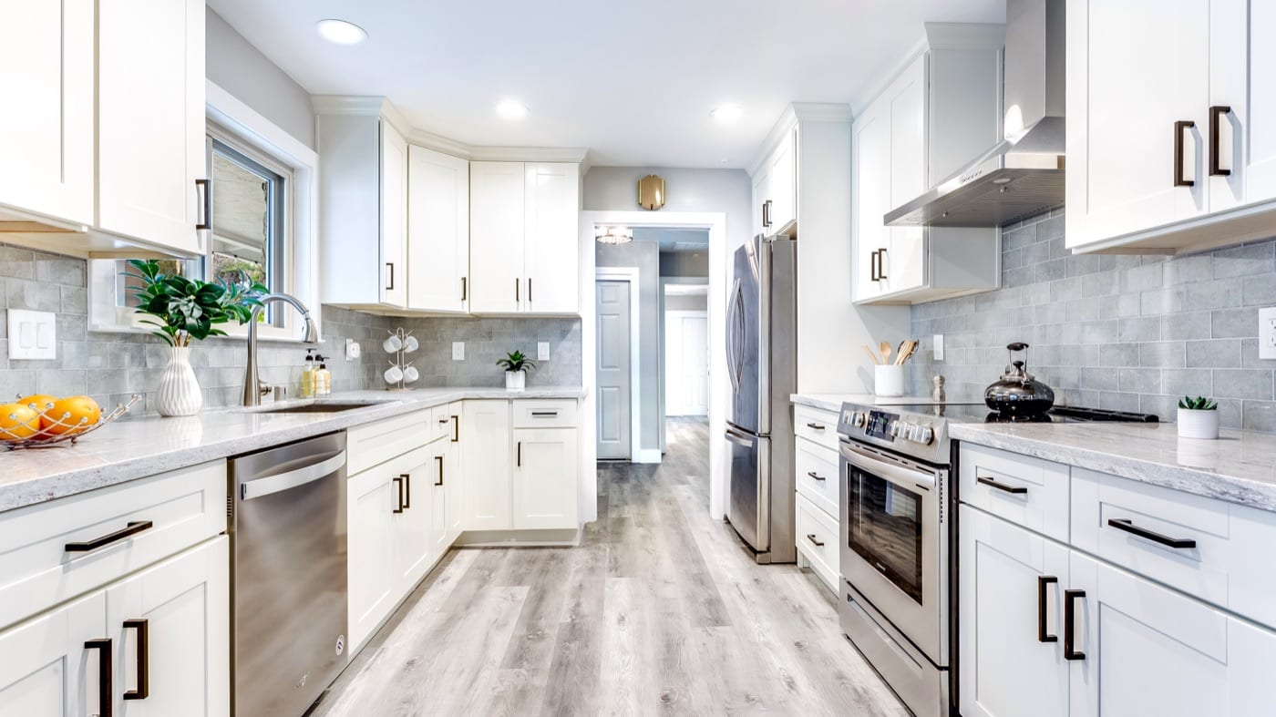 After: the same kitchen with white shaker cabinets, stone counters and new plank flooring