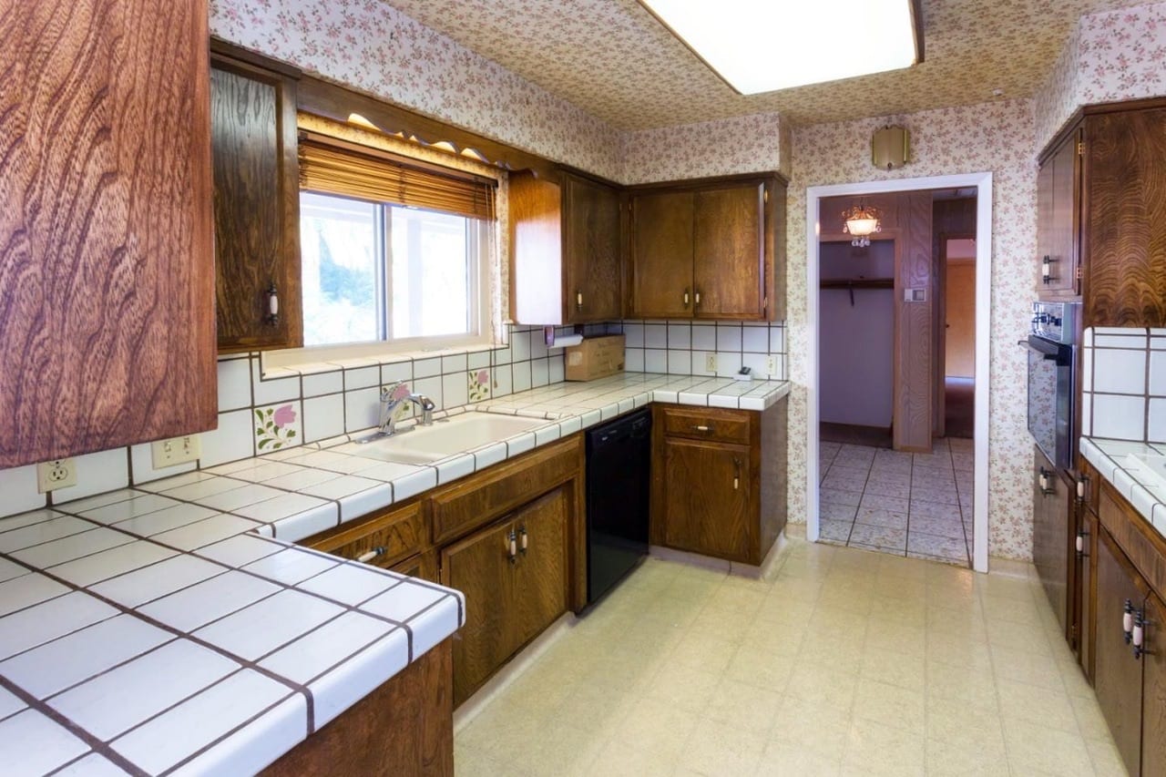 Before: original kitchen with dark oak cabinets, tile counters and floral wallpaper