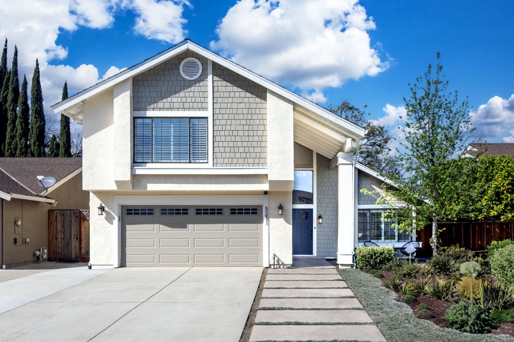 After: the same home repainted soft gray with white trim, a blue front door, a taupe garage door and new landscaping