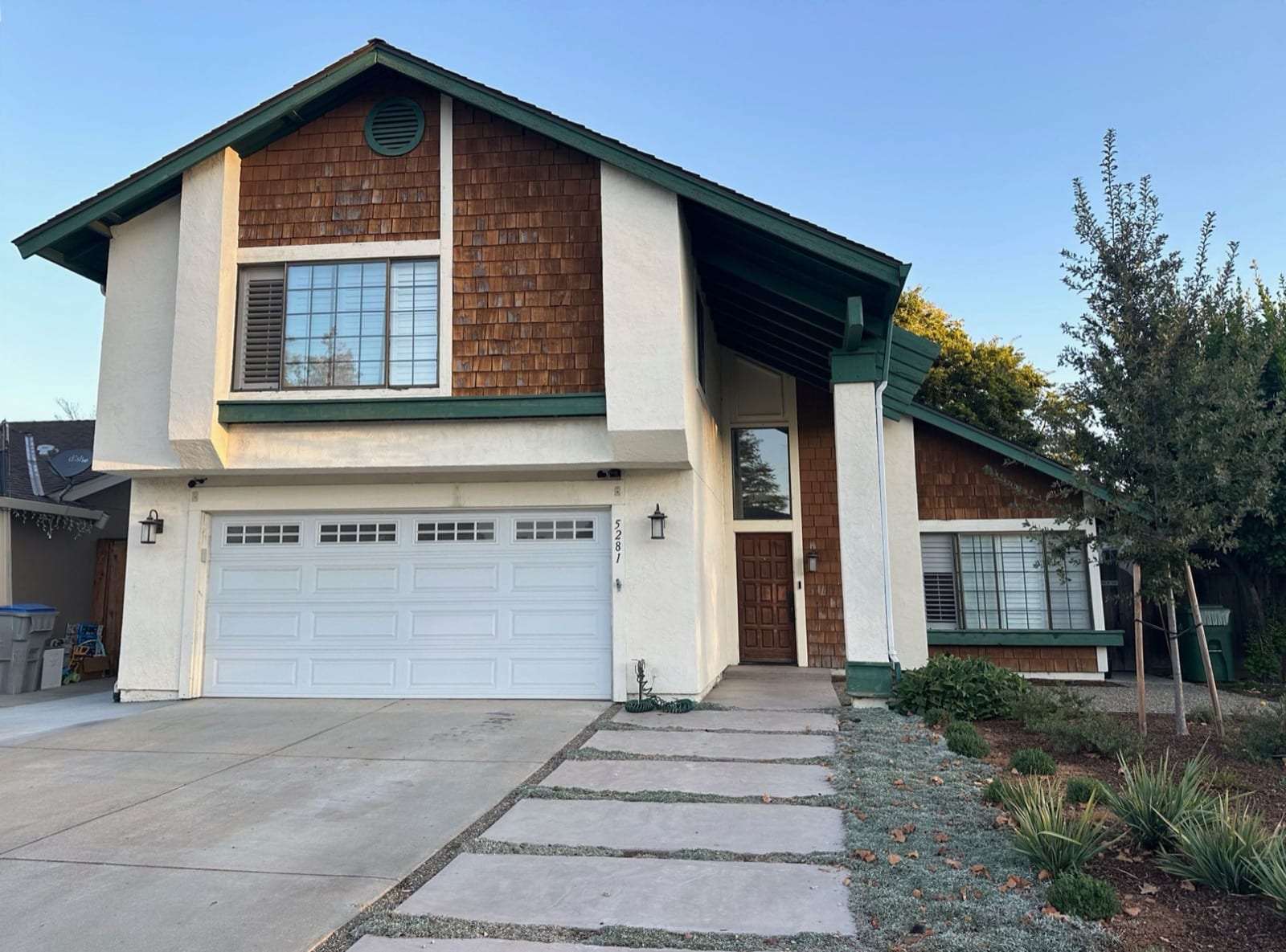 Before: two-story home with cedar shingle siding, green trim, a wood front door and a white garage door