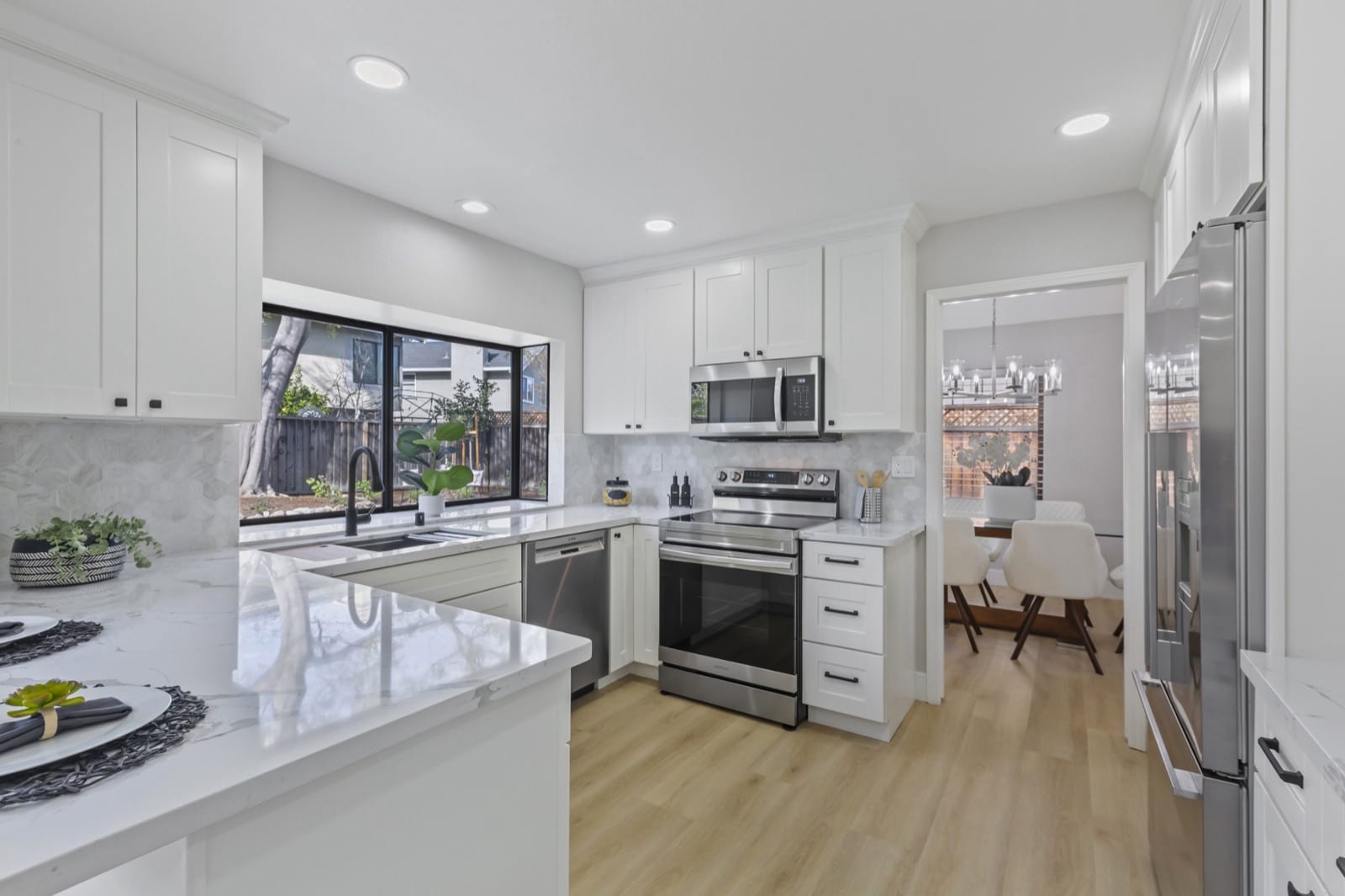 After: white shaker cabinets, new counters, a hexagon tile backsplash, a stainless range and light plank flooring