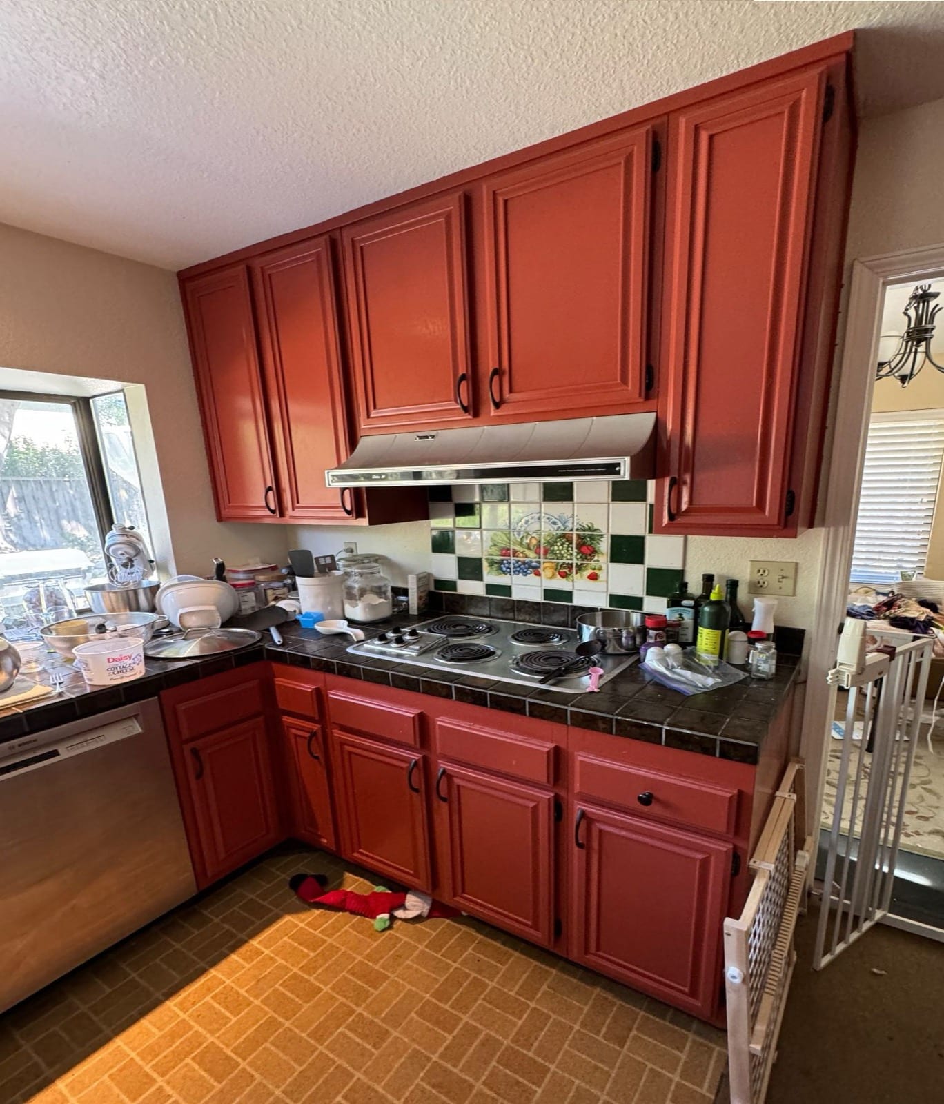 Before: red painted cabinets, an electric coil cooktop, tile counters and a fruit-motif tile backsplash