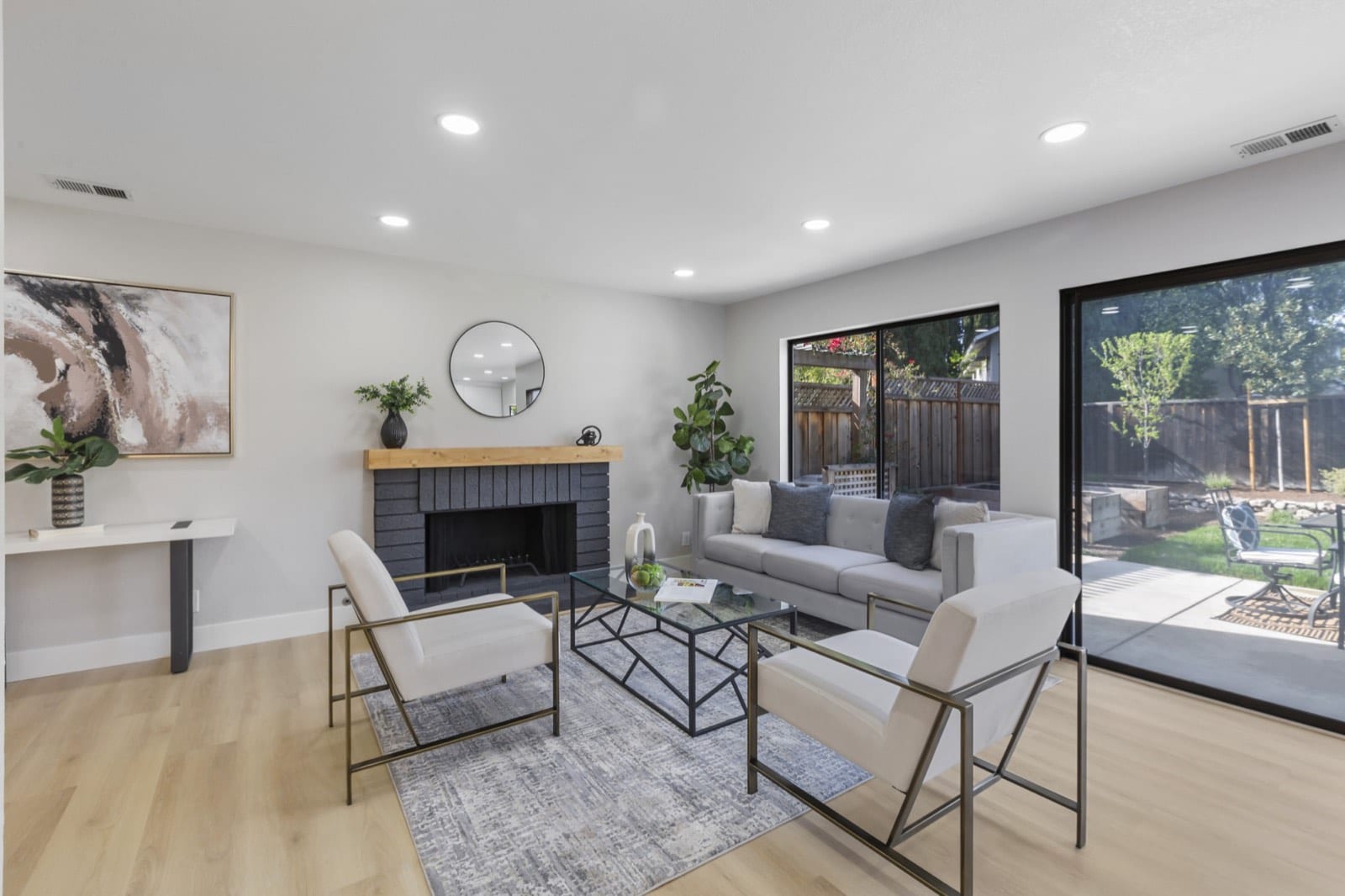 Family room with a brick fireplace and wood mantel, white chairs and sliding doors to the backyard