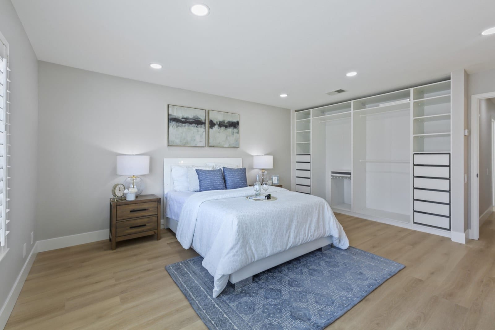 Primary bedroom with a queen bed, blue rug and a wall of built-in closet organizers