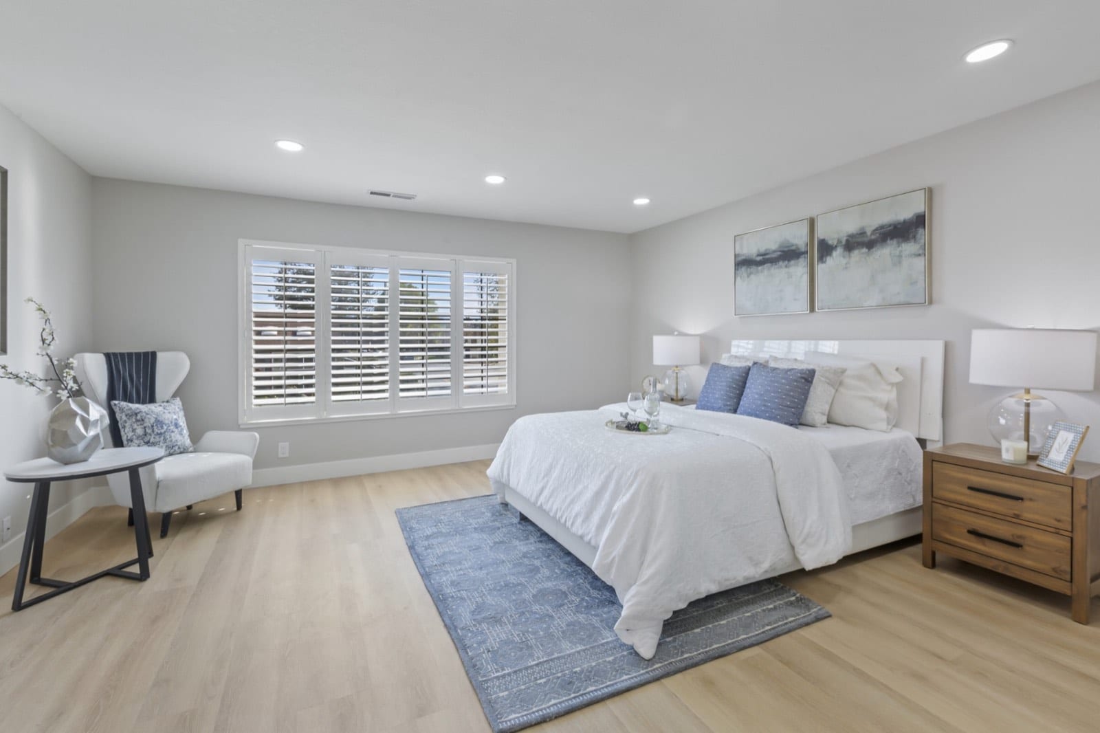Primary bedroom with plantation shutters, a reading chair and side table