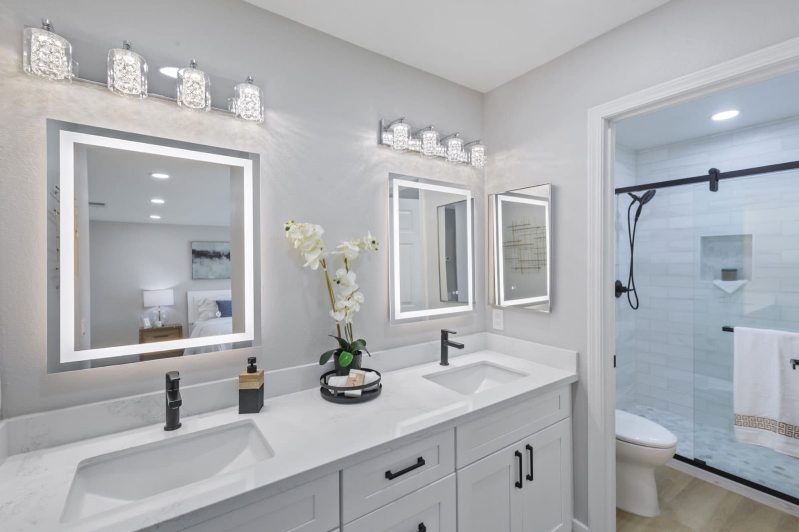 Primary bath with a double vanity, lighted mirrors, black fixtures and a glass shower