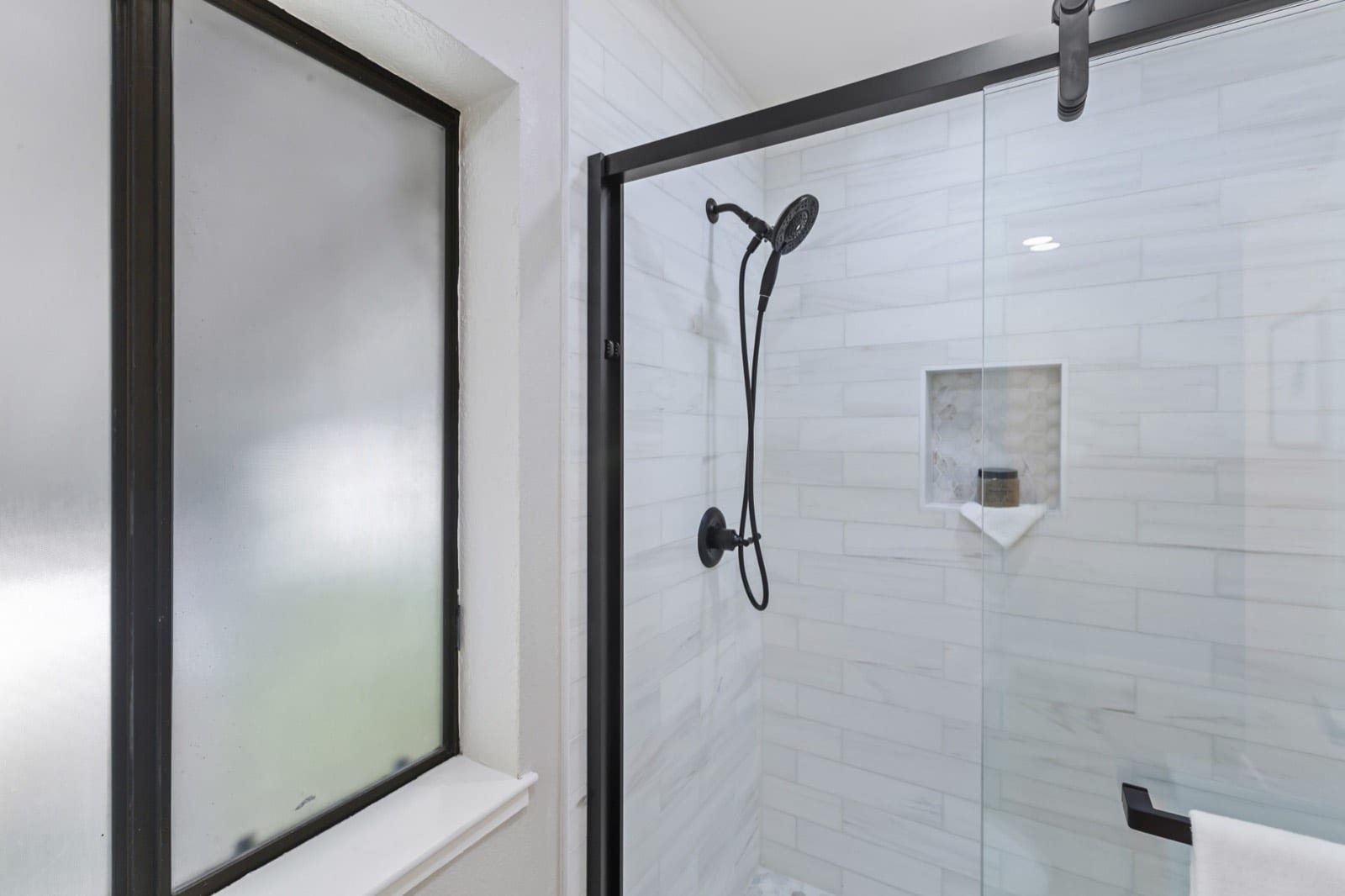 Walk-in shower with white marble tile, black fixtures and a mosaic niche