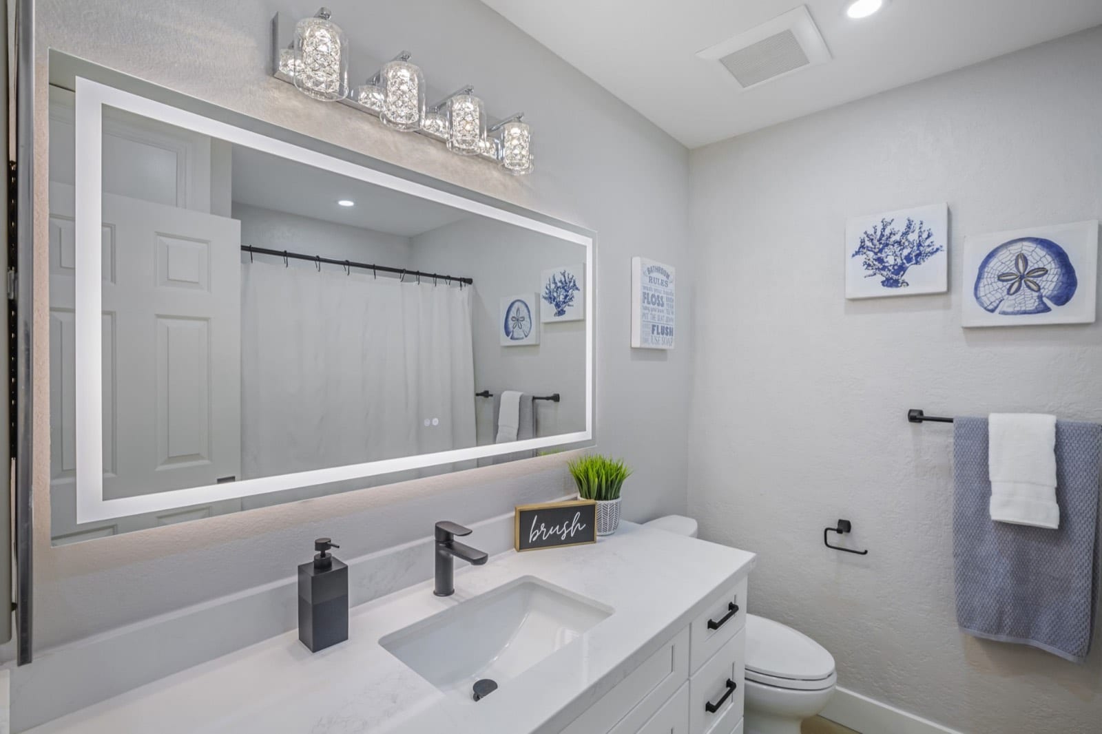Hall bath with a lighted mirror, black faucet and coastal art