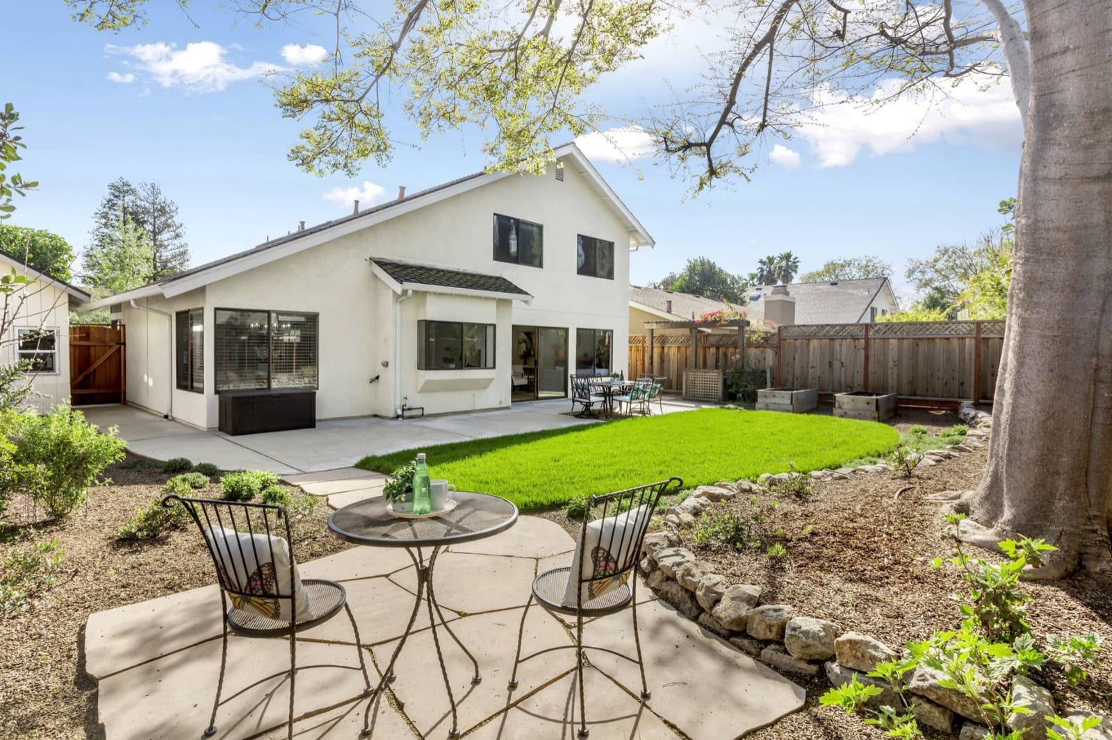 Backyard with a bistro set on flagstone, new lawn, raised garden beds and a patio dining area