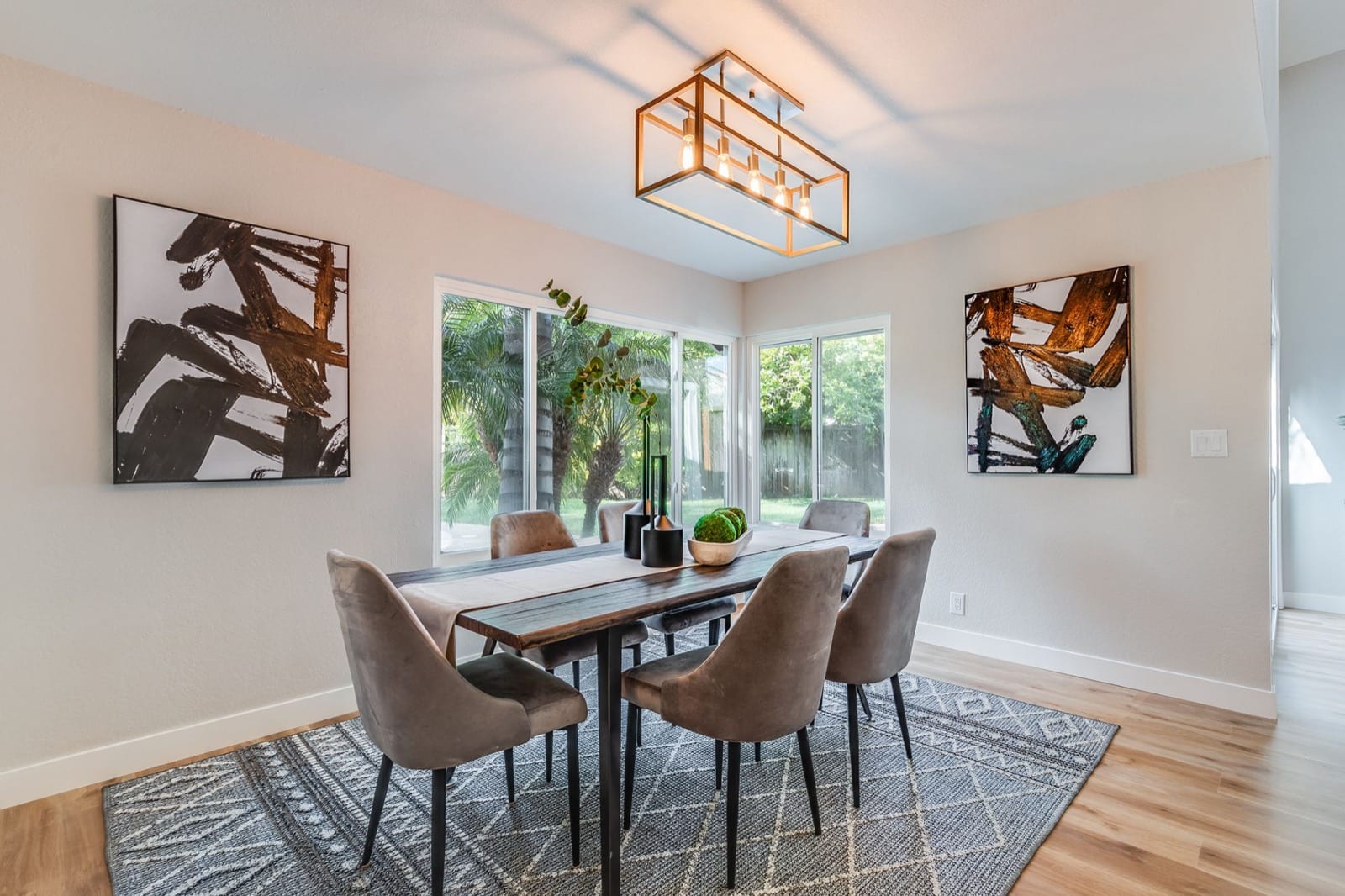 After: staged dining room with white walls, a modern chandelier and an open view of the palms and pool