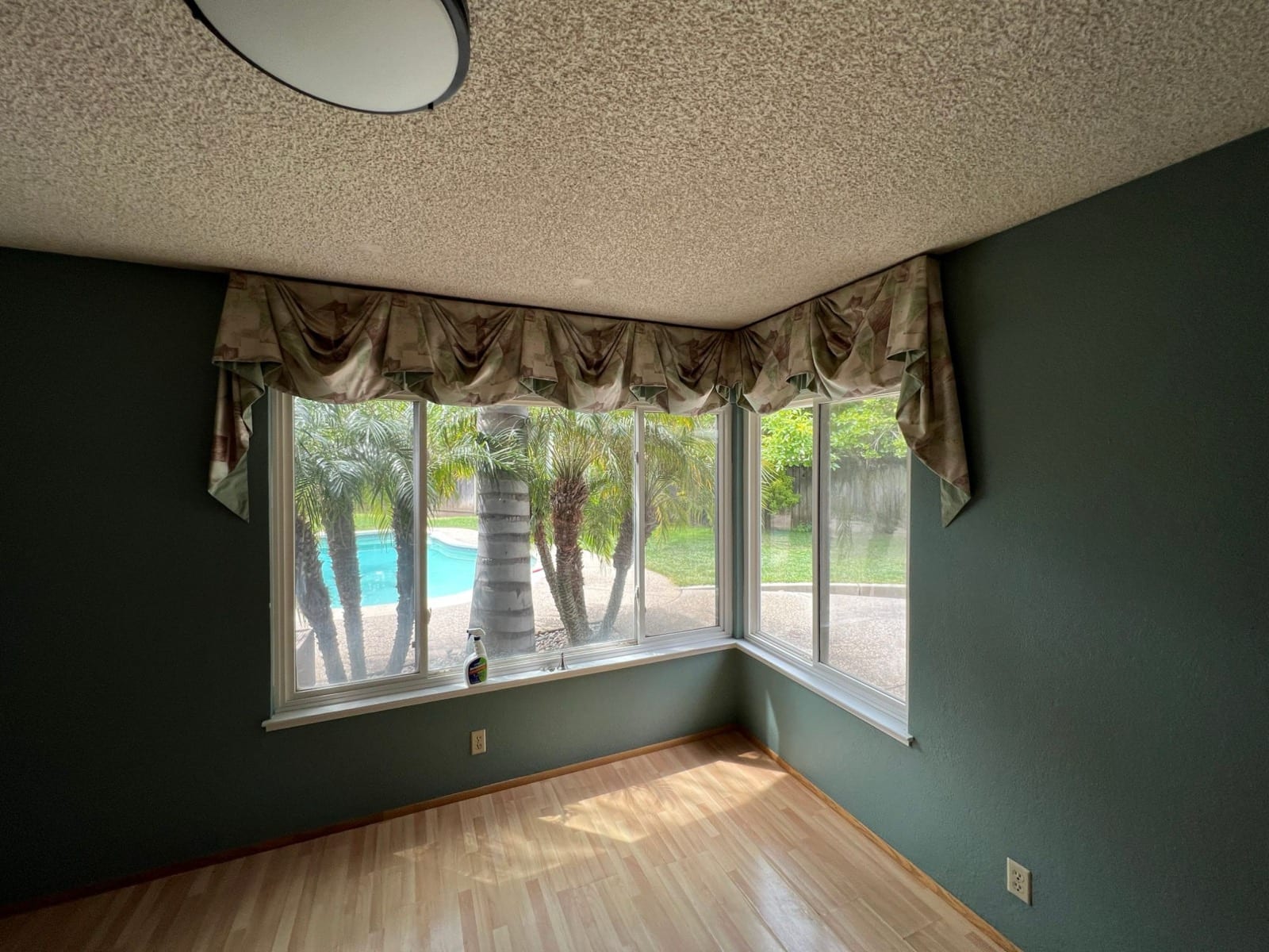 Before: empty dining room with forest green walls and a patterned swag valance over the windows to the pool