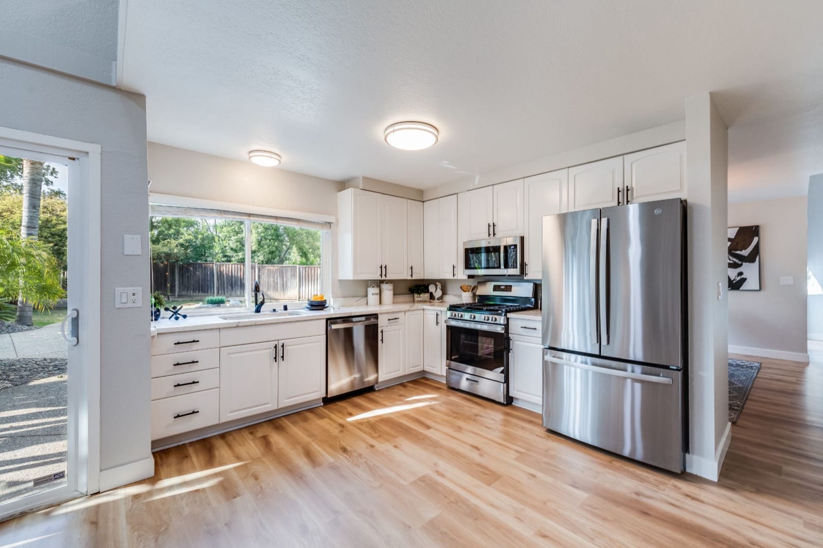 After: the same kitchen with white cabinets, new counters, stainless appliances and light plank flooring
