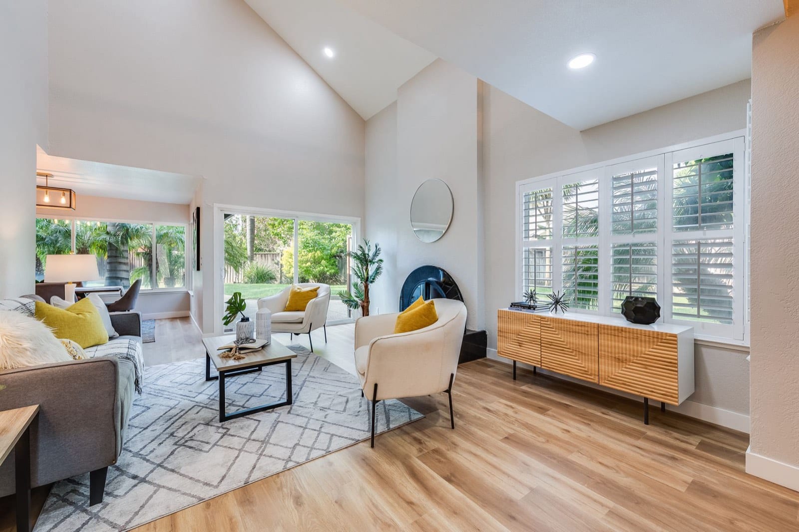 Vaulted living room with a fireplace, plantation shutters, light wood floors and a sliding door to the yard