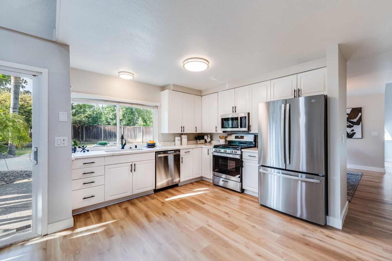 Updated kitchen with white cabinets, quartz counters, stainless GE appliances and a sliding door to the patio