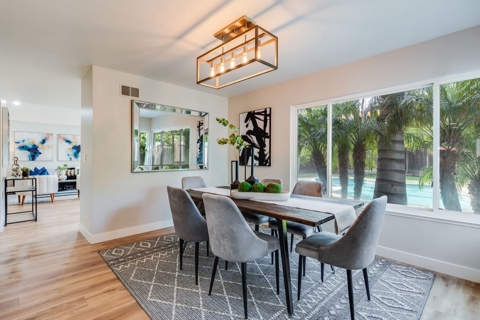 Staged dining room with a caged-bulb chandelier and windows onto the pool and palms