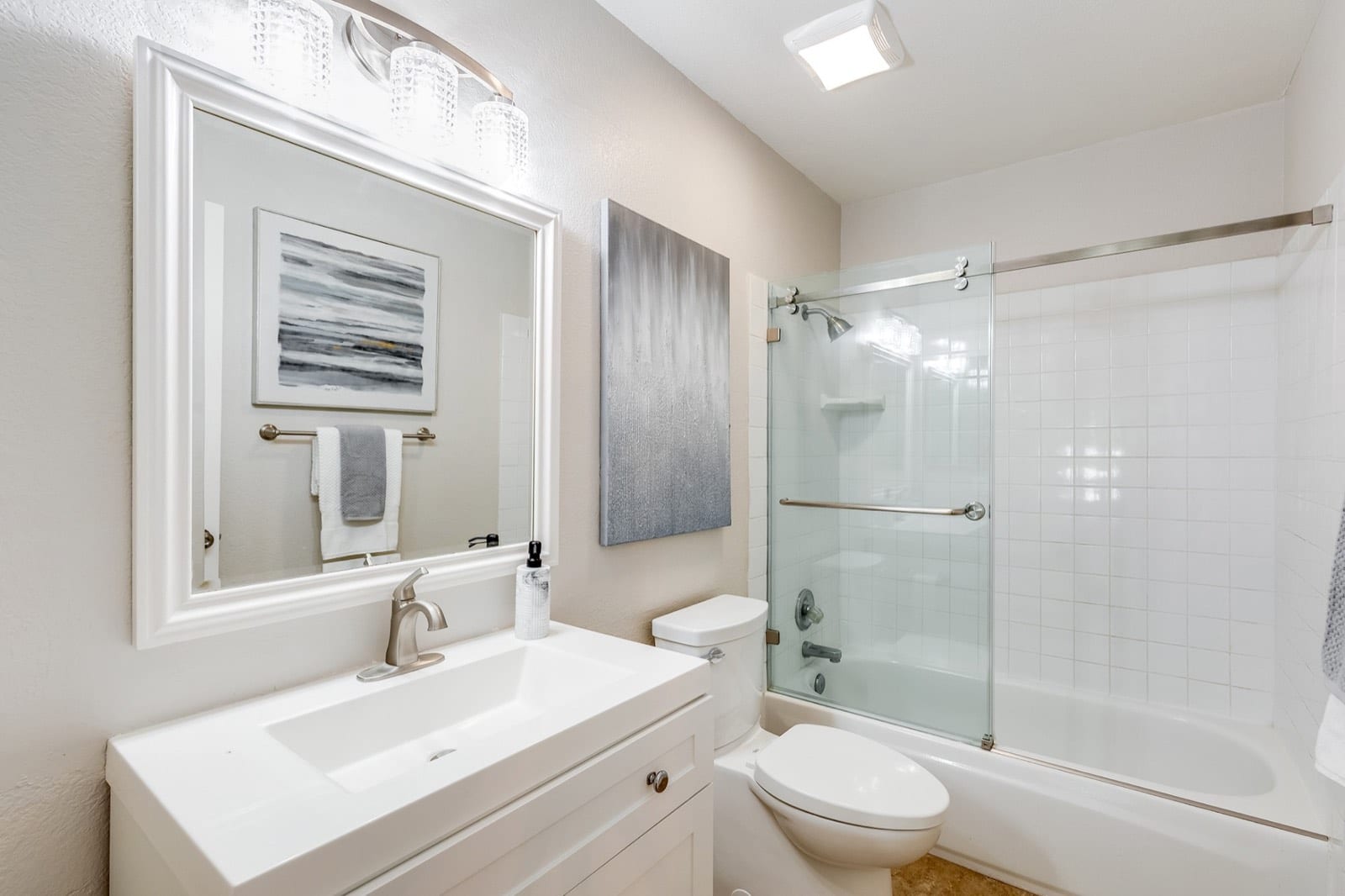 Hall bath with a white vanity, framed mirror and glass tub-shower doors