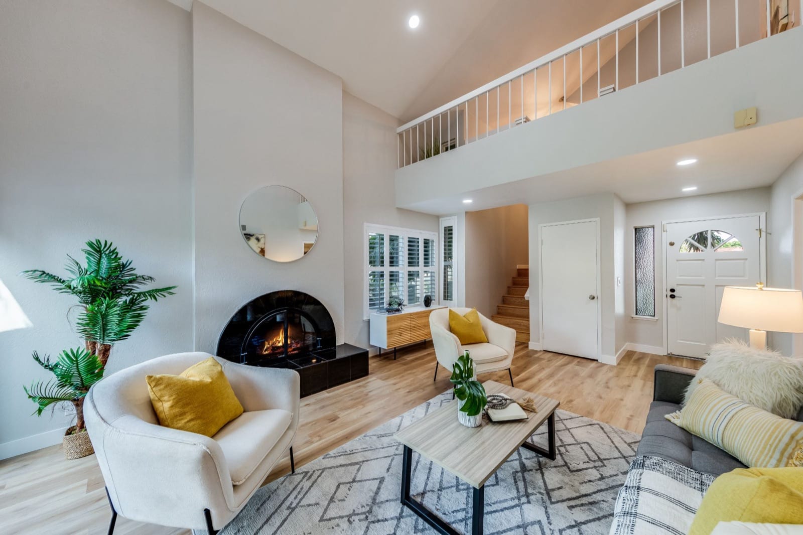 After: staged living room in soft neutrals with a fireplace, light plank flooring and a white loft railing