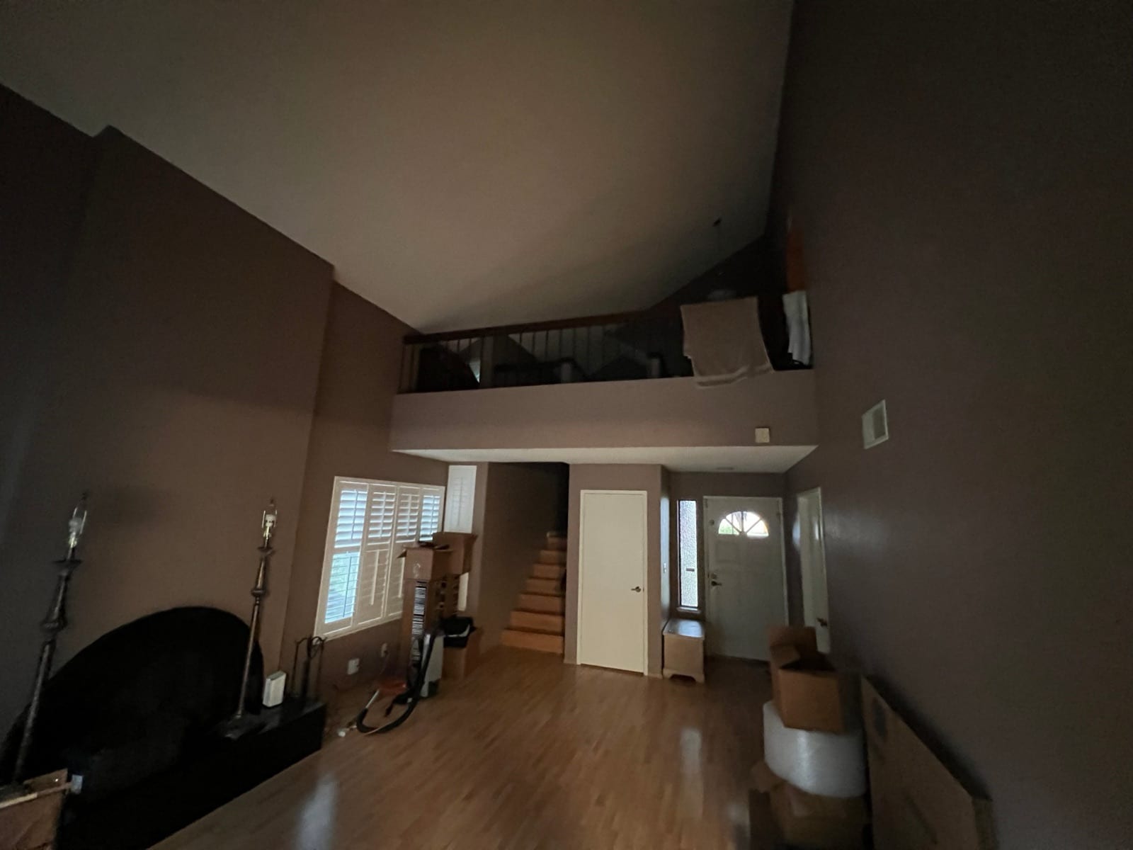Before: dark brown living room under a loft railing with moving boxes on the floor